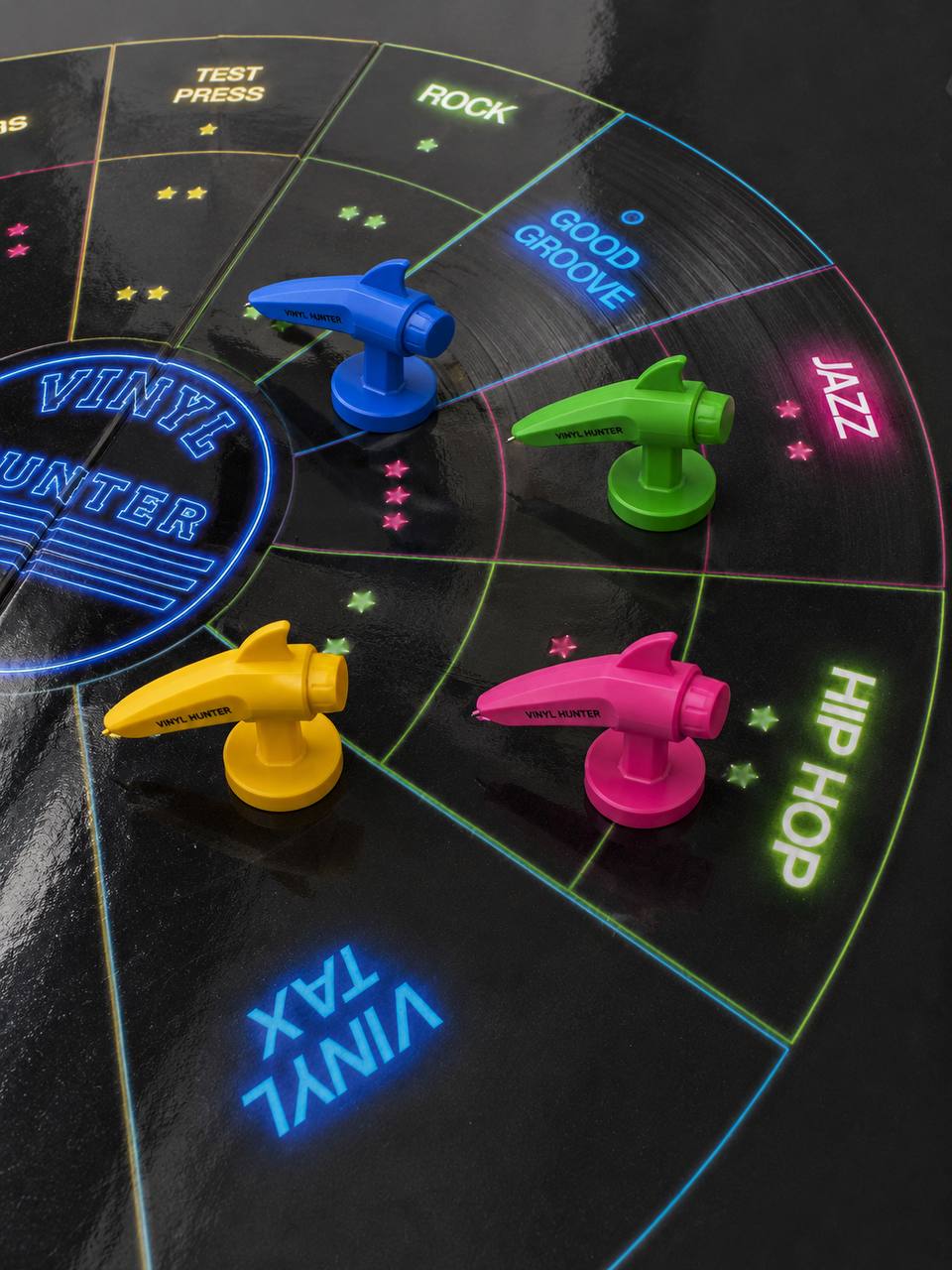 Vier Tonarm-Spielsteine auf dem Spielbrett – blau, grün, gelb und pink auf den Feldern Rock, Groove, Jazz und Hip-Hop